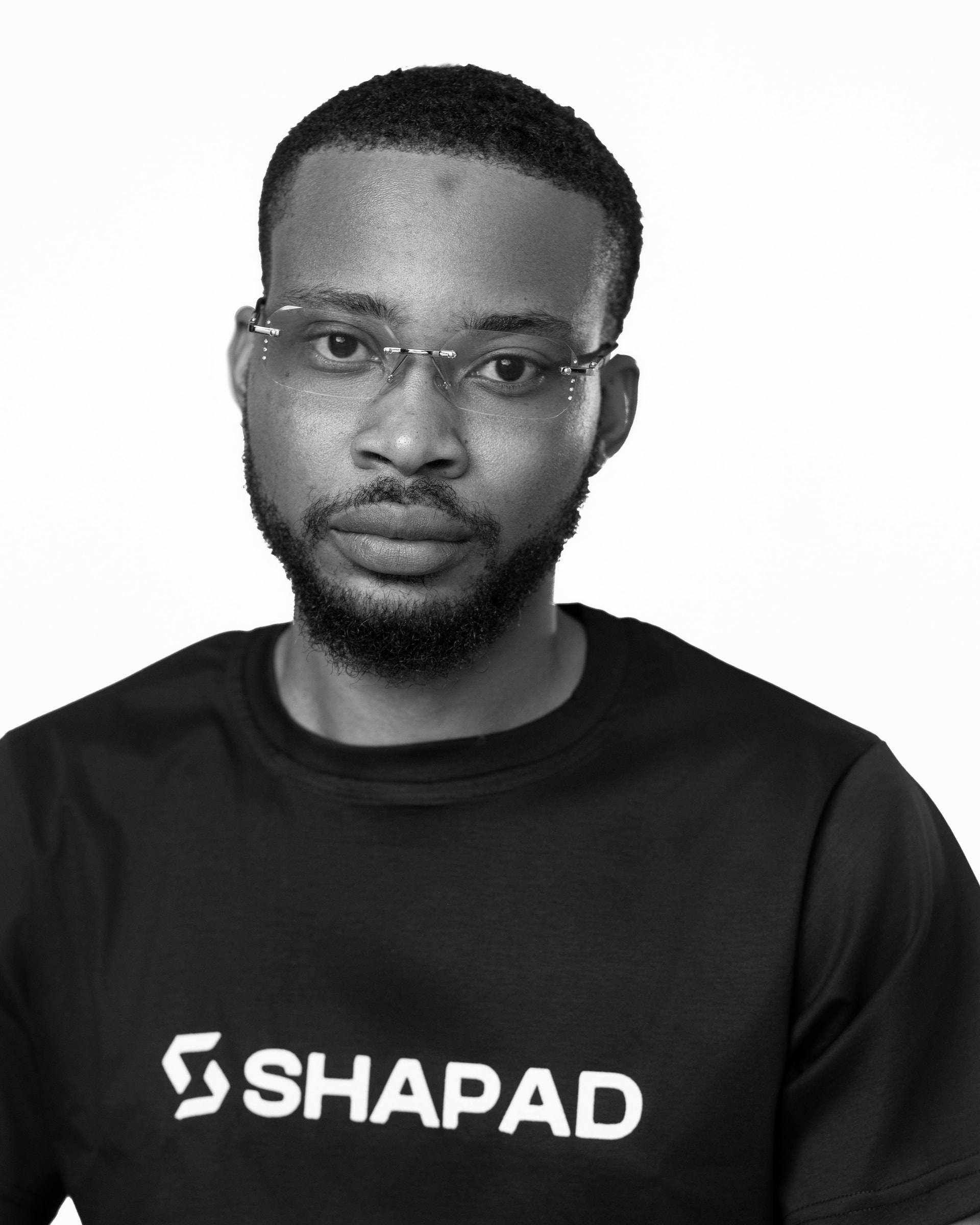 Close-up portrait of a Shapad team member in a black SHAPAD t-shirt, black-and-white studio photograph