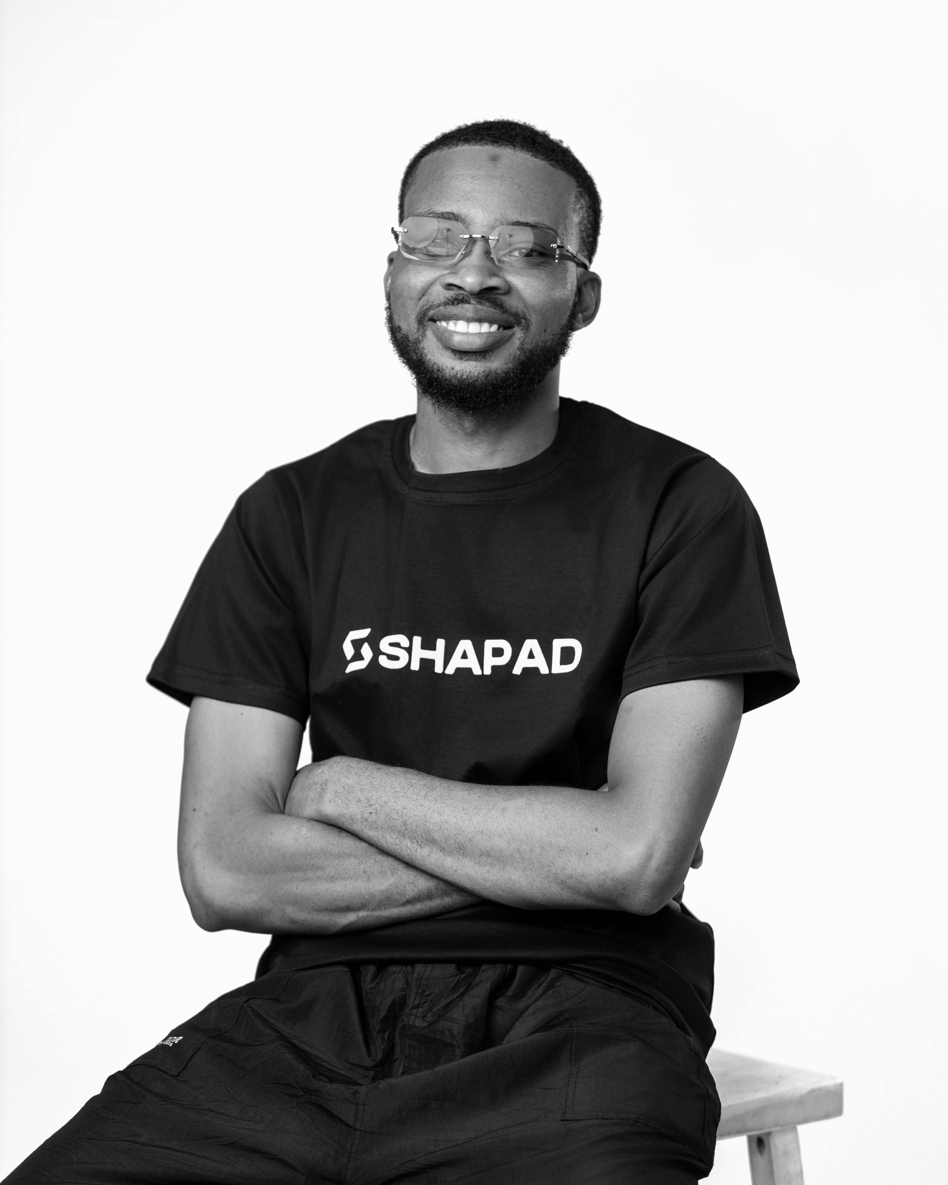 Member of the Shapad team in a black SHAPAD t-shirt smiling with arms crossed, black-and-white studio portrait